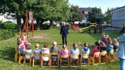 Policjantka prowadzi prelekcję dla przedszkolaków na placu zabaw dzieci siedzą na krzesełkach