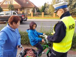 Policjantka wręcza odblaski chłopcu jadącemu z babcią rowerem drogą rowerową.