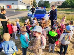 Policjantki prowadzą spotkanie z przedszkolakami.Spotkanie odbywa się na wolnym powietrzu dzieci stoją przed policyjnym radiowozem oznakowanym